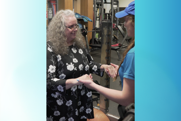 An older woman with white hair and glasses holding hands with her physiotherapist while they are doing a session.